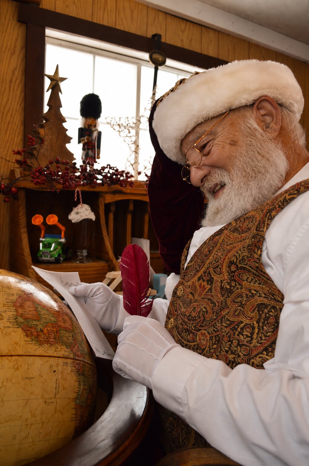 Santa writing a reply with a red feather quill beside his globe